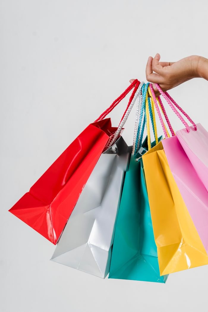 Close-up of a hand holding multiple colorful shopping bags on a white backdrop, perfect for retail or consumerism concepts.